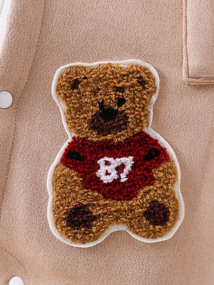 Détail du patch ourson brodé en relief sur la barboteuse bébé beige