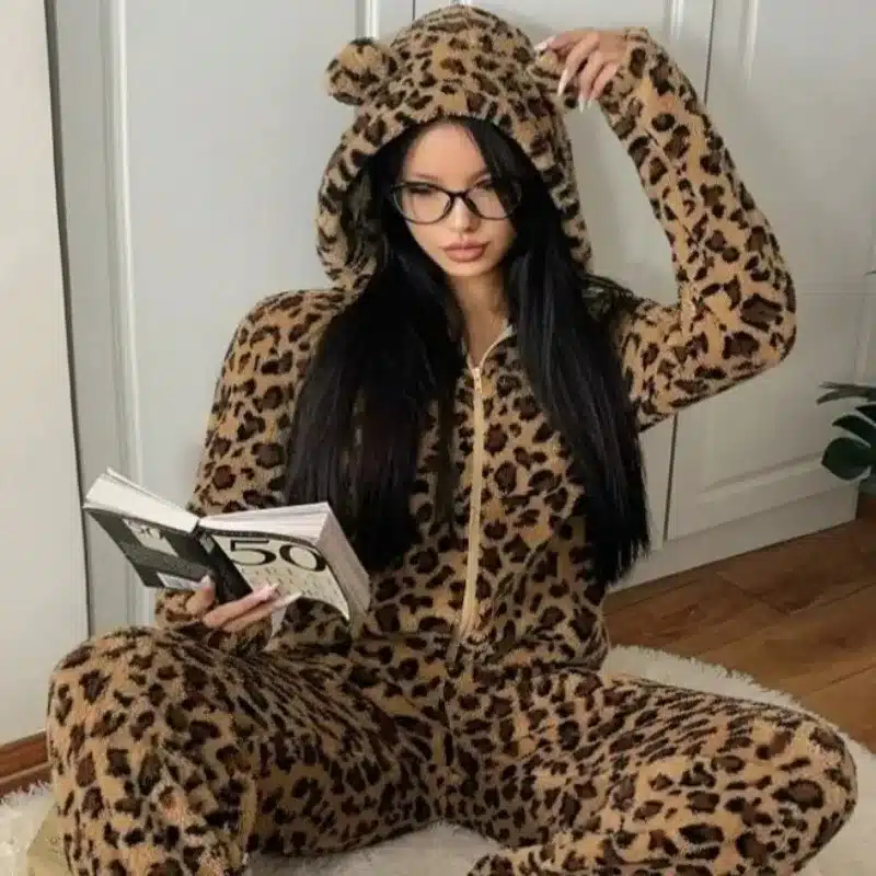 Femme portant une combinaison pyjama léopard à capuche en polaire, assise avec un livre
